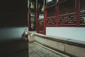 A close-up of a black door with a brass ring handle, opening to reveal a red lattice window and a...