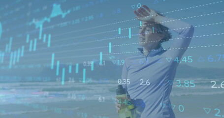 Image of graphs, loading circles, trading board, tired caucasian athlete standing at beach