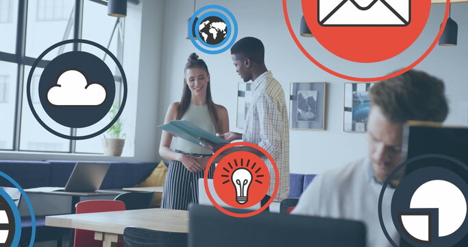 Image of icon in circles over diverse coworkers standing and discussing reports in office