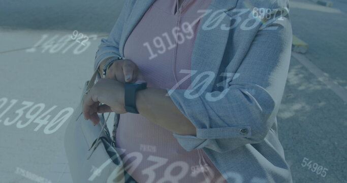 Image of multiple changing numbers over biracial woman standing and using smartwatch