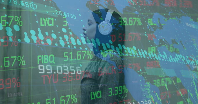 Image of graphs, map, trading board, biracial woman wearing hijab listening to music