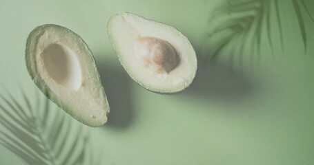 Naklejka premium Image of palm tree leaves over halved avocado on green background