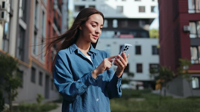 A happy woman in casual clothing uses her phone on a city street