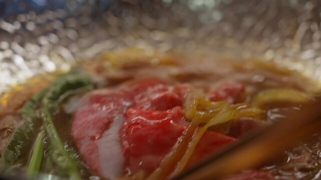 Close-up of A5 beef slices in a silver hot pot with sukiyaki broth, highlighting the marbled texture and rich, savory broth. Perfect for showcasing the premium quality of the beef and the delicious.