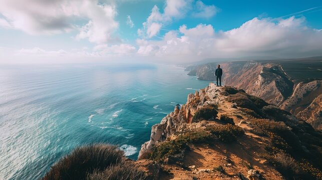 The view from a mountain top in the Algarve region of Portugal offers a breathtaking panorama of the ocean, where azure waters meet rugged coastal cliffs under a clear sky.