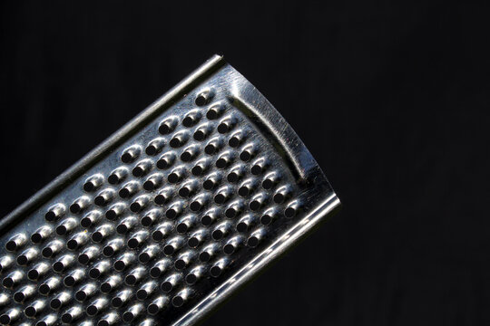 Close up of a metal grater kitchen utensil against a black background