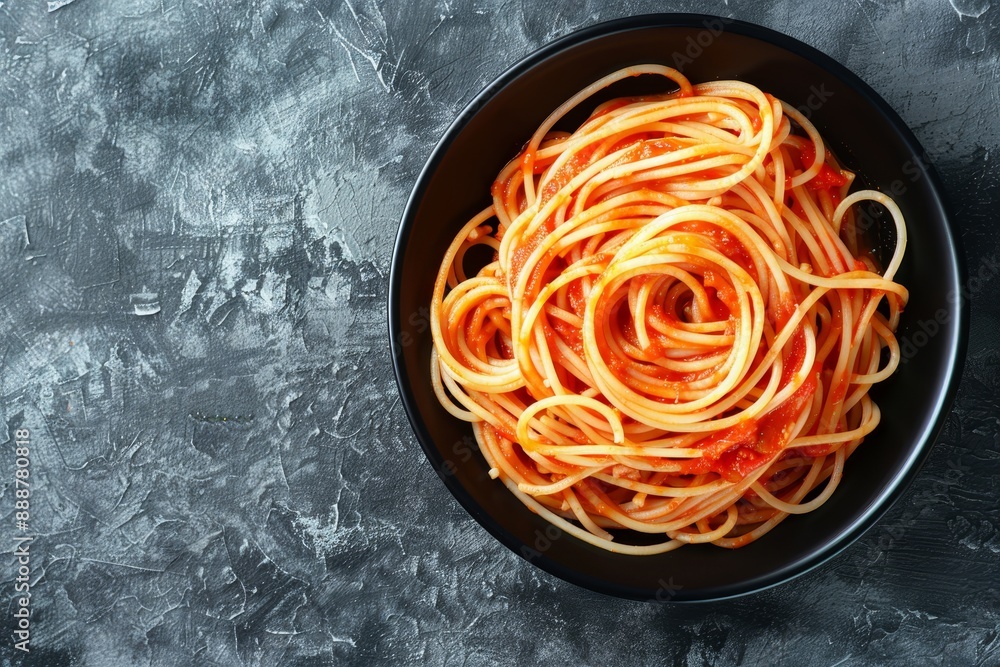 Wall mural top view of spaghetti in black bowl with tomato sauce on grey stone background