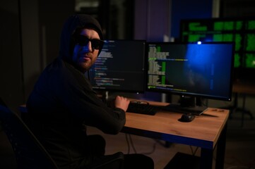 hacker sitting at desk in dark atmosphere. A computer programmer or hacker. Anonymous computer hacker.