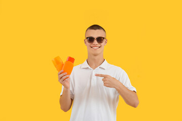 Happy young man in sunglasses pointing at bottles of sunscreen cream on yellow background