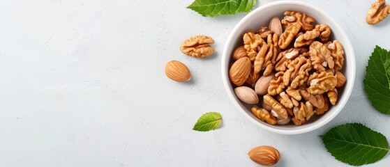 Fototapeta premium A white bowl holds nuts and a green leaf on a white surface An individual green leaf lies nearby