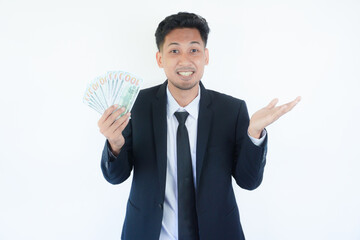 Excited young Asian business man 20s wearing suit standing hold fan of cash money in dollars banknotes spreading hands isolated