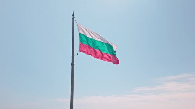 Raised unfurled Bulgarian flag flys symbolically patriotic in breeze with sky backdrop