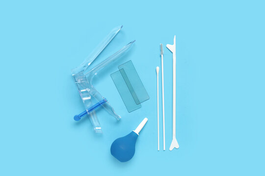 Gynecological speculum with pap smear test tools and enema on blue background