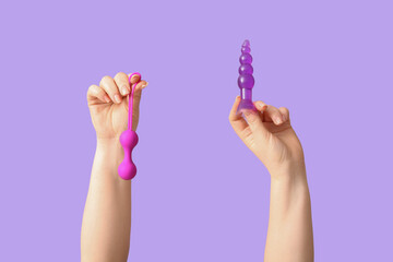 Female hands with sex toys on lilac background, closeup
