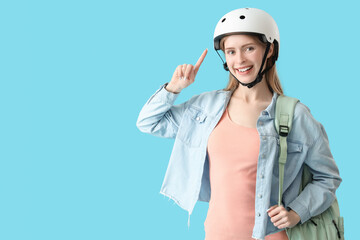 Beautiful young woman pointing at helmet on blue background
