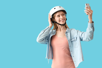 Beautiful young woman in helmet taking selfie on blue background