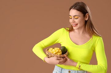 Beautiful young woman holding wicker basket with sweet mango fruits on brown background