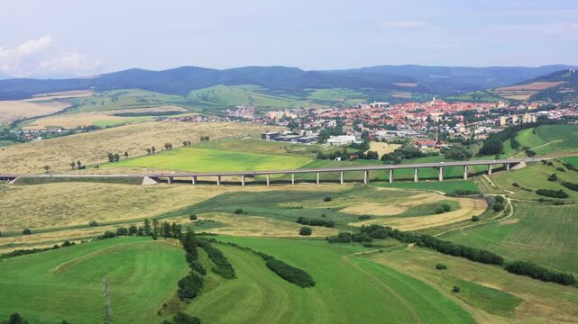 Drone shot of European route E50 highway road infrastructure through green agricultural fields landscape connecting European continent, Levoca town in background
