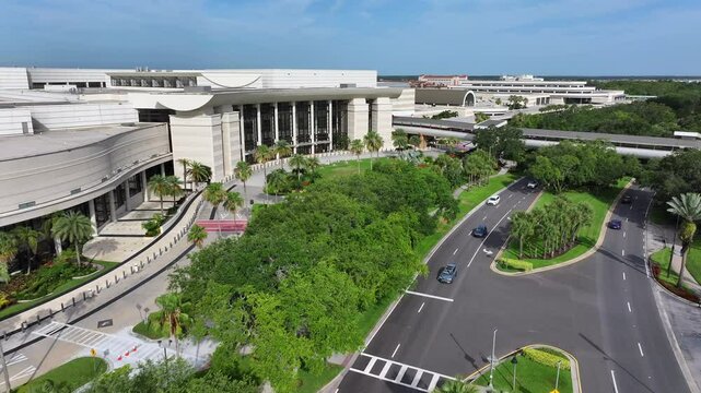 Modern Orange County Convention Center in Orlando with tropical neat garden park. Bridge and cars in street. Sunny day with blue sky. Aerial flight along complex building in Florida, USA.