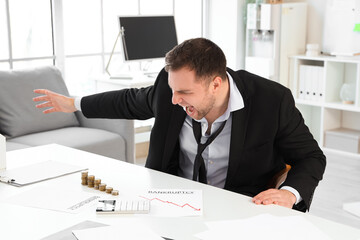 Angry bankrupt businessman with stacks of coins on table in office