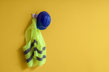 Safety vest and hardhat hanging on yellow wall