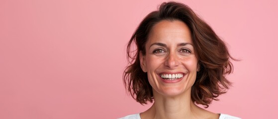  A smiling woman with brown hair wears a white T-shirt, gazing at the camera against a pink backdrop