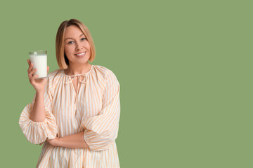 Happy young woman with glass of fresh milk on green background