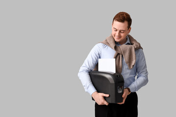 Handsome young man holding shredder on grey background