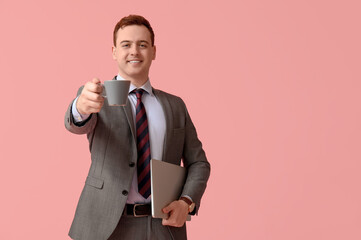 Naklejka premium Young man with laptop and cup of fresh coffee on pink background