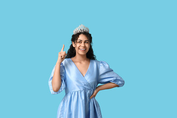 Pretty young African-American woman pointing at beautiful tiara and stylish dress on blue background