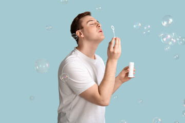 Young handsome man blowing soap bubbles on blue background