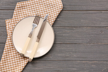 Table setting with plate, cutlery and checkered napkin on grey wooden background