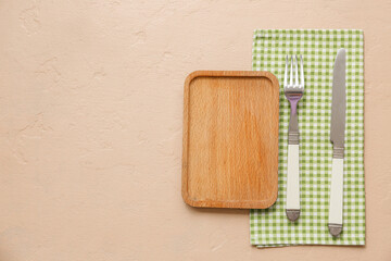 Table setting with wooden board, cutlery and napkin on beige background