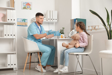 Male pediatrician talking to little girl at table in clinic