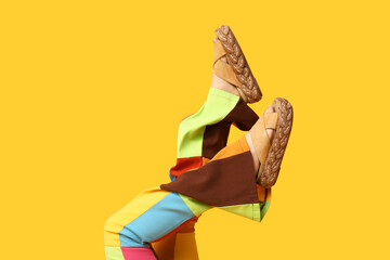 Legs of young woman in trousers and sandals on yellow background