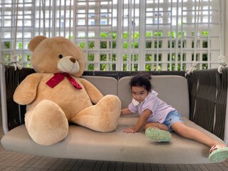 Cute little girl with teddy bear sitting on sofa at home