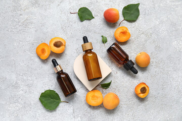 Bottles of cosmetic oil with fresh apricots on grey background