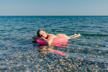 A woman is floating on a pink inflatable tube in the ocean