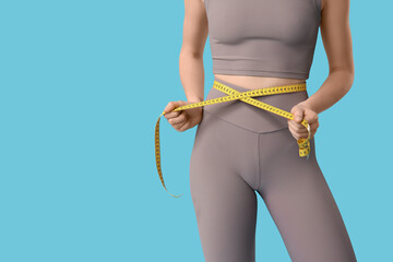 Sporty young woman with measuring tape on blue background. Diet concept