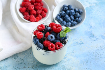 Glass of tasty yogurt with different fresh berries and mint on light blue background