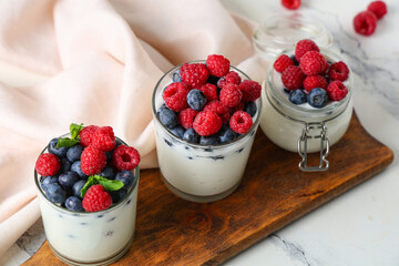 Glasses and jar of tasty yogurt with fresh blueberries and raspberries on white background