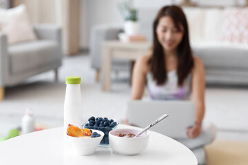 Sporty young Asian woman with laptop at home, focus on tasty yogurt and fruits on table