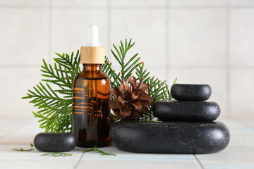 Composition with bottle of essential oil, spa stones and thuja branch on light tile background