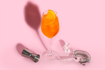 Glass of Aperol spritz cocktail with ice cubes on pink background