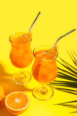 Glasses of Aperol spritz cocktail and palm leaf on yellow background