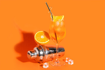 Glass of Aperol spritz cocktail and shaker on orange background