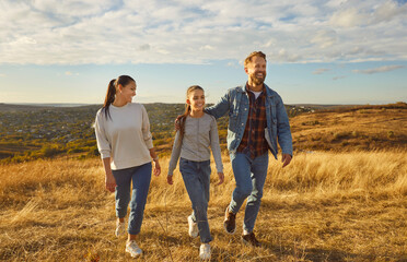 Happy smiling young family with child girl walking in the field enjoying nature at sunset. Mother, father and their teenage daughter spending time outdoors. Family leisure concept.