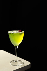 Green unique alcoholic cocktail with basil flavor in a tall glass on a dark background decorated with a flower. Palm leaves. Summer evening, relaxation, nightlife. Bar, restaurant.
