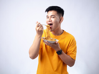Chinese Indonesian man in yellow shirt picking up fried noodles with fork from a white plate, while...