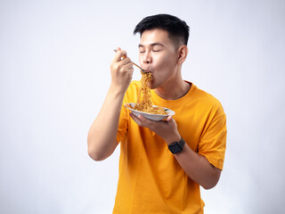 Chinese Indonesian man in yellow shirt picking up fried noodles with fork from a white plate, while...